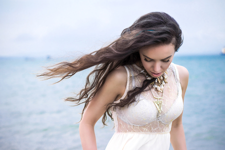 Beautiful young brunette woman outdoors portrait near the sea looking downの写真素材