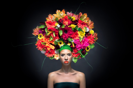 Beauty Girl with Flowers Hairstyle. Beautiful Young Woman Portrait with Summer orange Flowers. Big hat with flowers, Fashion Makeup. Orange lipgloss.の写真素材