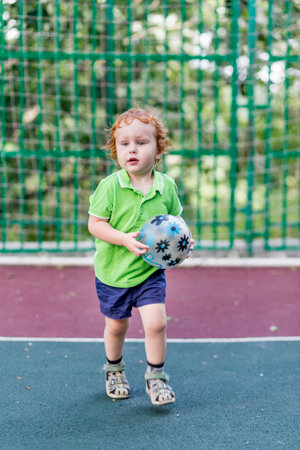 A little boy 2 years old plays ball on the sports field. The kid plays football on the playground. Sports kid and childhood concept.の写真素材