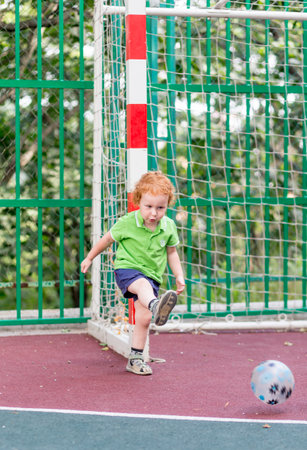 A little boy 2 years old plays ball on the sports field. The kid plays football on the playground. Sports kid and childhood concept.の写真素材