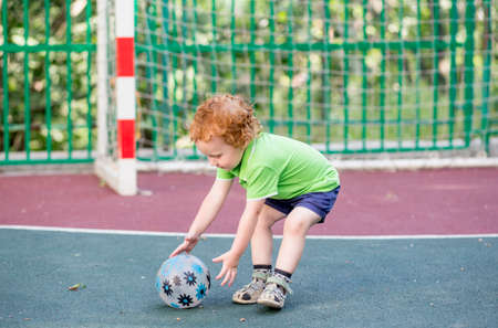 A little boy 2 years old plays ball on the sports field. The kid plays football on the playground. Sports kid and childhood concept.の写真素材