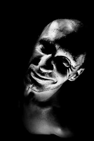 Portrait of adult caucasian man. He smiles like maniac and seems madness. Black and white shot, low-key lighting. isolated on black.の写真素材