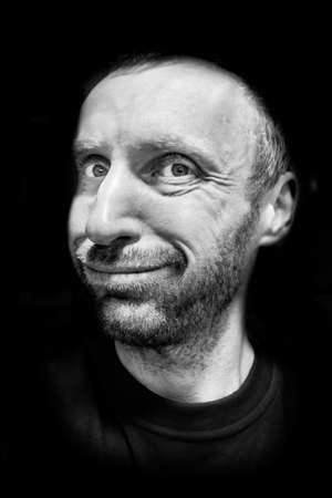 Portrait of adult caucasian man with funny smile. Low key lighting. isolated on black.
