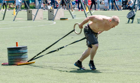 Russia, Vladivostok, June 01, 2019. A strong athlete performs a dog sled exercise with heavy weights. Power sports and fitness concept.の写真素材