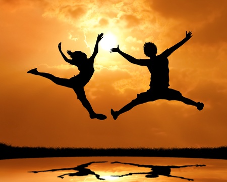 silhouette of man and woman jumping and touch the sunの写真素材