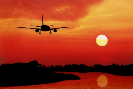 silhouette of plane fly over land and river during sunrise
