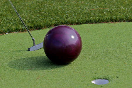 Golfer trying to putt a bowling ball into the cup の写真素材