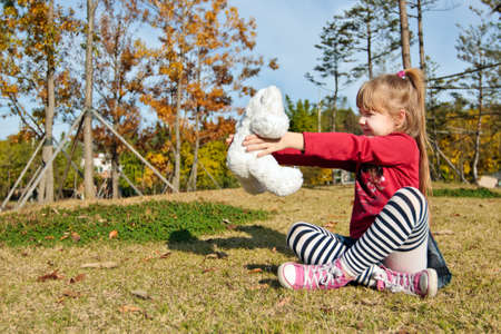 Little girl with a toy sitting on a grass in autumn parkの写真素材
