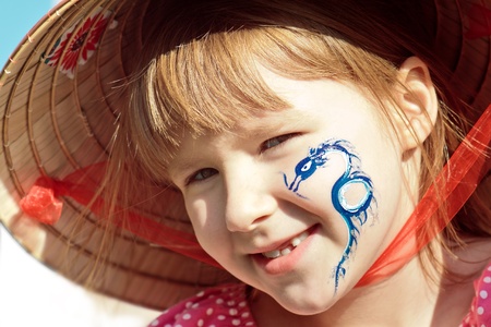 Portrait of a happy girl with a dragon painted on her cheek