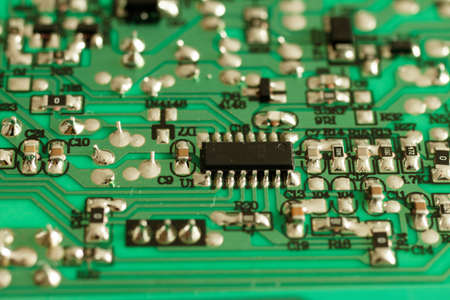 Close up of an electronic component on a green circuit board with deep bokeh