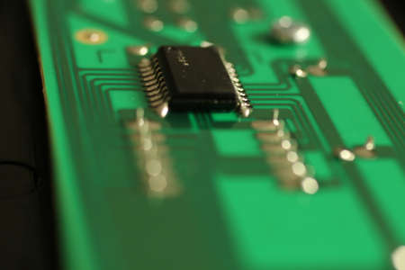 Close up of an electronic component on a green circuit board with deep bokeh