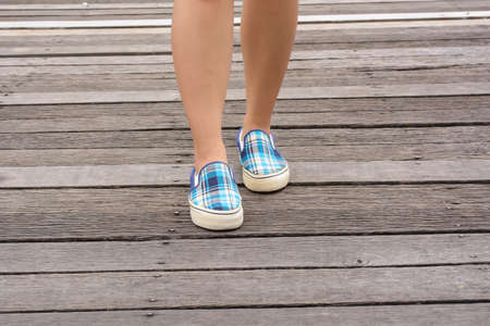 Girl wearing canvas sneakers standing on the wooden bridge.