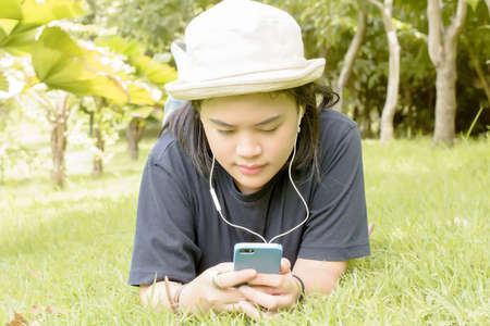 Young woman listening to music from your smart phone on the grass in the park.の写真素材