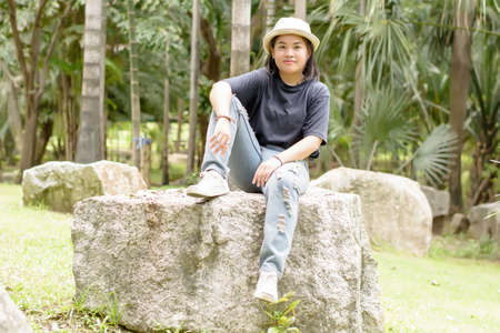 Young woman sitting on a big rock in the park.の写真素材