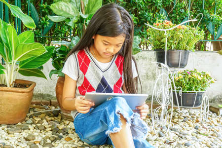 The girl sitting in mini garden with playing tablet pc.の写真素材
