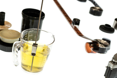 A setup for developing photographic film with a measuring cup, yellow liquid, reels, and...