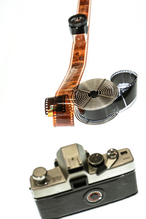 Vintage camera and long film strip coiled through a reel on a white background.