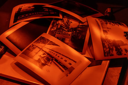 A set of black-and-white photographic prints being processed under a red safelight in a darkroom....