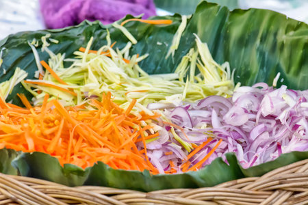 Trays of shredded green papaya, carrots and sliced red onions on banana leaf.の写真素材