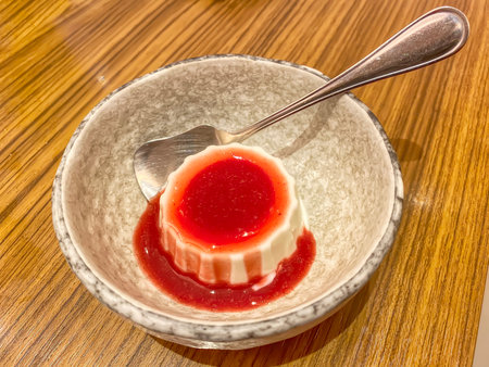 Delicious white panna cotta pudding topped with red strawberry sauce in ceramic bowl.の写真素材