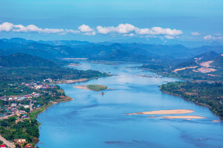 Stunning aerial view of the Mekong River meandering through mountains, sandbars, forests, and rural towns under a bright blue sky.の写真素材