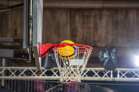 A yellow and blue basketball is caught in motion just above the hoop during an indoor game.の写真素材