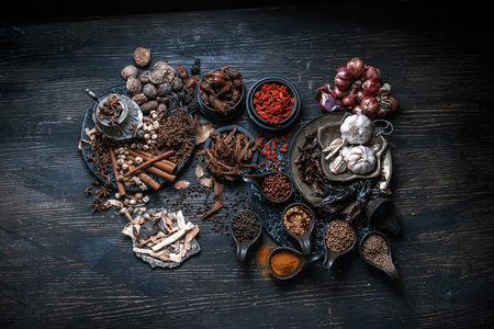 Collection of various dried spices and herbs arranged on dark wooden table.の写真素材