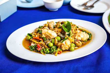 Authentic Thai spicy stir fried fish with green peppercorns and herbs on white plate.の写真素材