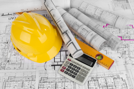 Yellow helmet, calculator, level and project drawings