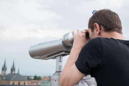 man carefully looking through binoculars at landmarks of town