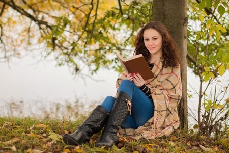 Attractive brunette young woman with book in the park in the autumnの写真素材