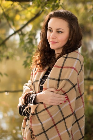 Attractive brunette young woman with blanket in the park in the autumnの写真素材
