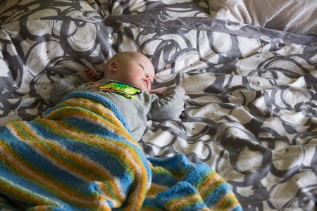 Cute baby boy with Down syndrome sleeping on the bed in home bedroomの写真素材