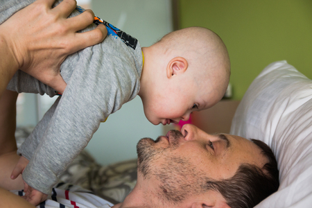 Cute baby boy with Down syndrome playing with dad on the bed in home bedroomの写真素材
