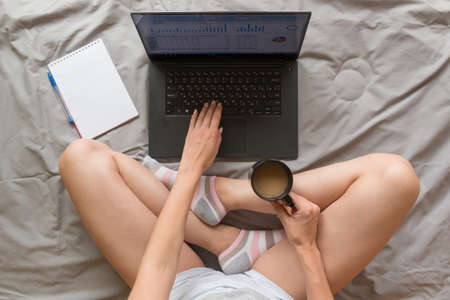 Home office concept: girl working with laptop and morning coffee in bed at homeの写真素材