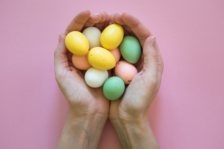 Colorful easter eggs in hands on pink background