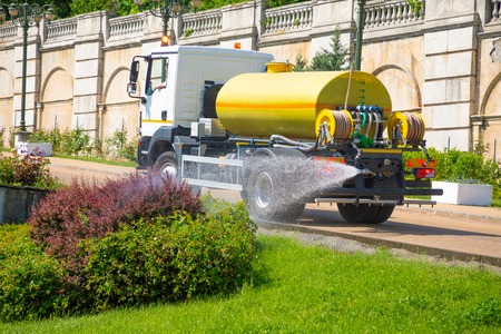Yellow truck watering trees in public park.
