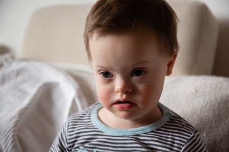 Portrait of cute small boy with Down syndrome in home living roomの写真素材