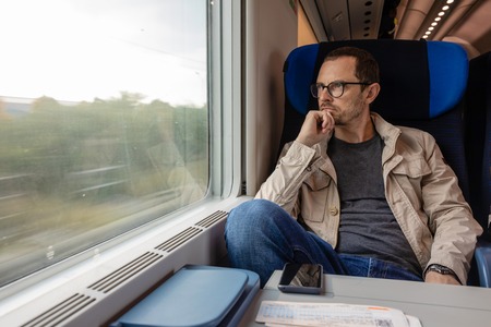 Middle age man looking out of the window of train. Passenger during travel by high speed express train in Europeの写真素材