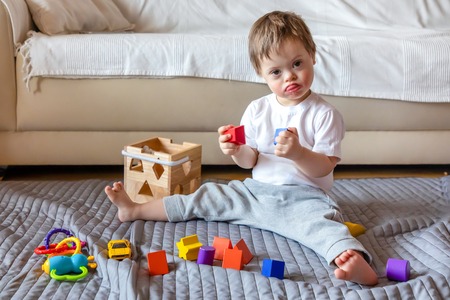 Cute small boy with Down syndrome playing with toy in home living roomの写真素材