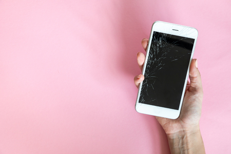 White smartphone with broken screen in hand on pink backgroundの写真素材