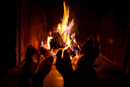 Bare legs of young woman and man are heated by an open fire in fireplace