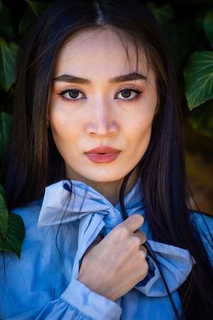 Portrait of young stylish asian woman in green leaves on stone wall backgroundの写真素材