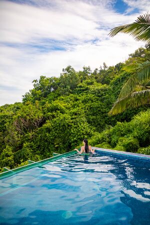Woman relaxing in infinity swimming pool with sea view, vacation in tropical country