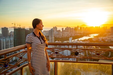 Young woman looks at view of Sanya city with river at sunset light in Hainan province, China