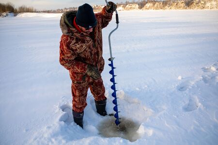 Kemerovo, Russia - 23.02.2019: A fisherman drills a hole in the ice to catch fish, Tom river in Kemerovo in Russiaのeditorial素材
