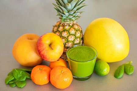 Different tropical fruits and green smoothie in glass on grey background, healthy eating lifestyle conceptの写真素材