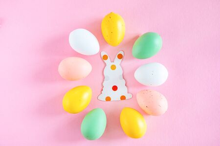 Colorful easter eggs and paper silhouettes of an easter bunny on pink background with text copy...