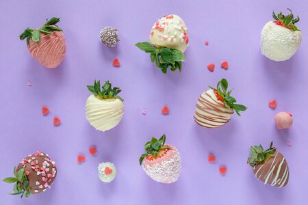 Variety of handmade colorful chocolate covered strawberries with different toppings on purple backgroundの写真素材