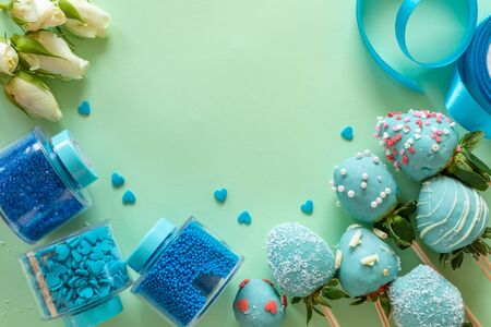Blue handmade chocolate covered strawberries, flowers and decoration for cooking dessert on green background with free space for textの写真素材